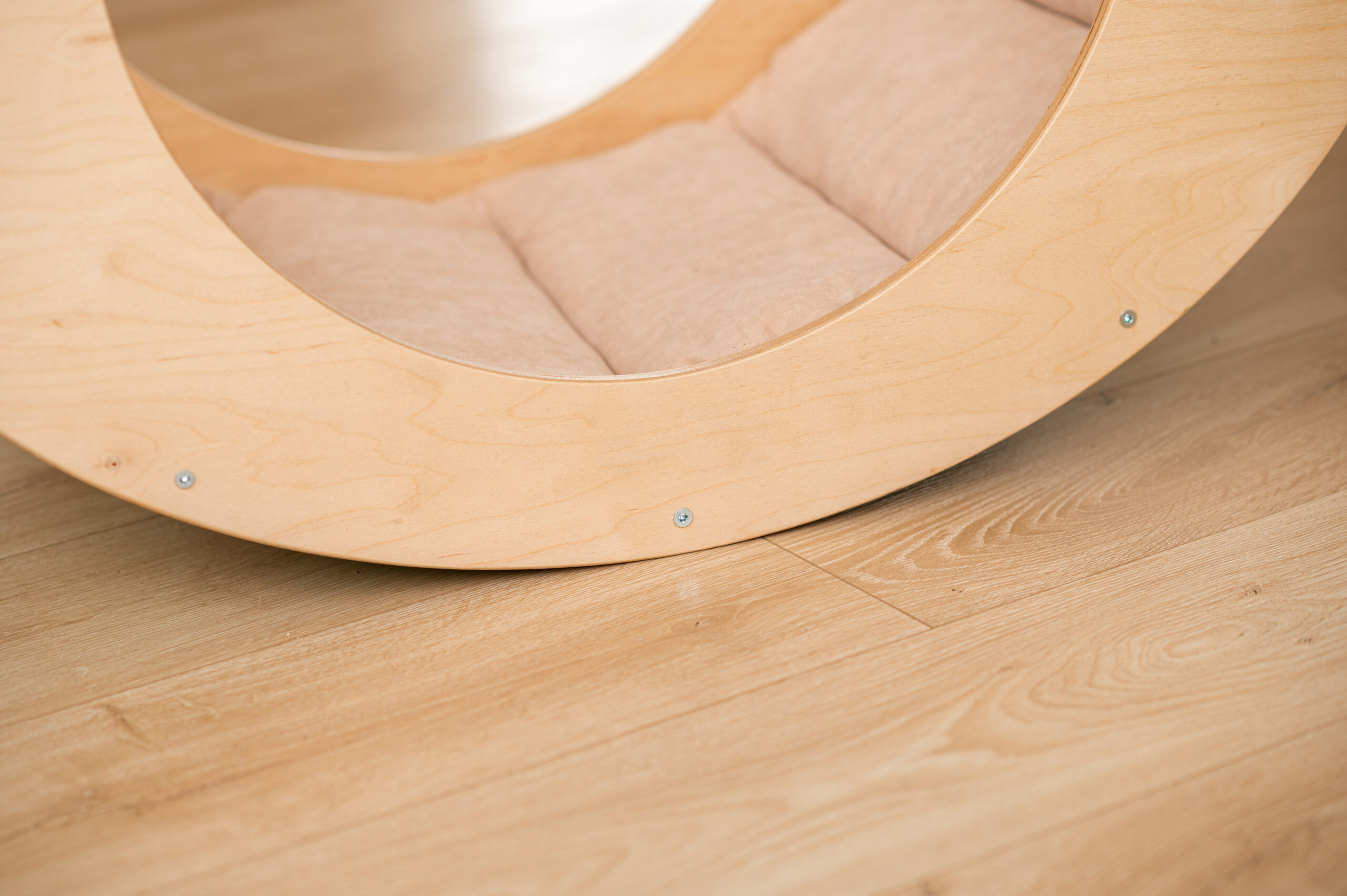 A light wood rocking chair frame with a padded seat, standing on a light wood floor.